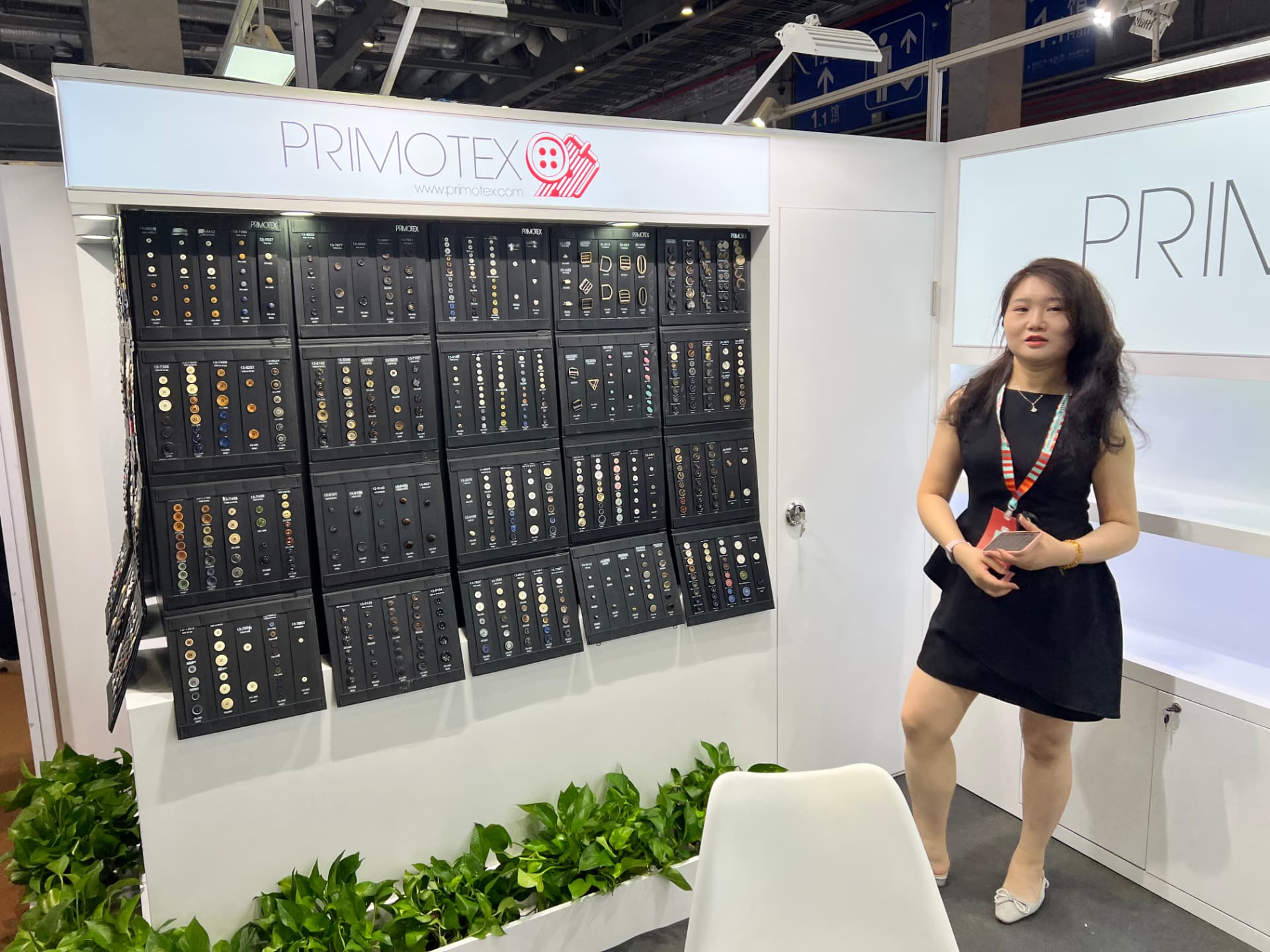 Primotex team member standing in front of the button sample wall at the booth