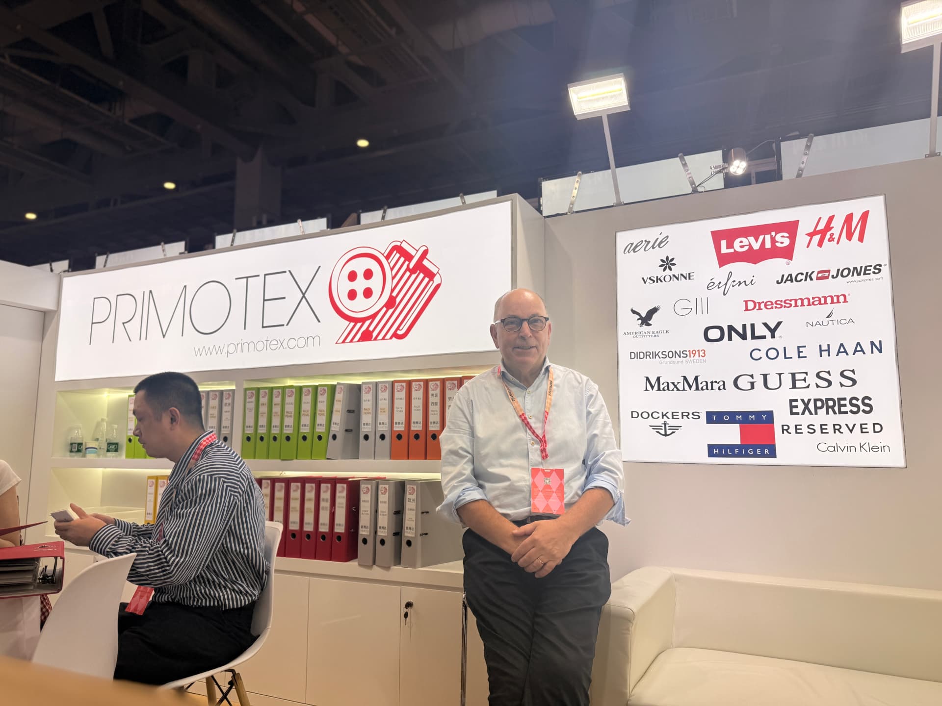 Primotex team member standing in front of the Primotex sign and customer logo wall